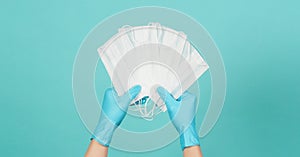 Hands holding white mask or face masks wear blue medical gloves or latex gloves on green and blue or mint background