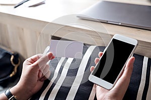 Hands holding white mobile phone with blank black desktop screen and a white empty business card