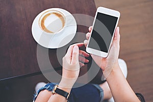 Hands holding white mobile phone with blank black screen with coffee cup on wooden table and floor background