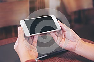 Hands holding white mobile phone with blank desktop screen with laptop computer on the table