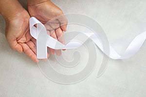 Hands holding white pearl ribbon bow on white fabric with copy space. Lung Cancer Awareness, Mesothelioma and Retinoblastoma photo