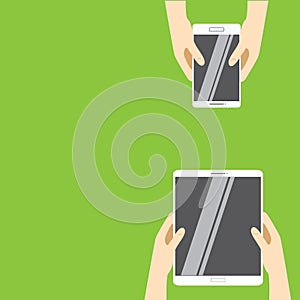 Hands holding white tablet computer and white smartphone on a green background.