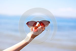 Hands holding women`s sunglasses on the background of the blue sea and the sun