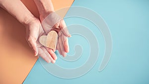 Hands holding wood heart on blue and orange colors paper background.