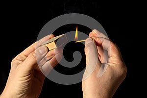Hands holds a burning match on a black background. A wooden match burns in the hands of a macro. Igniting a match on a box. Smoke