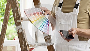 Hands of house painter man decorator choose the color using the sample swatch, work of the house to renovate, use mobile phone, a photo