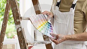 Hands of house painter man decorator choose the color using the sample swatch, work of the house to renovate, a wooden ladder and