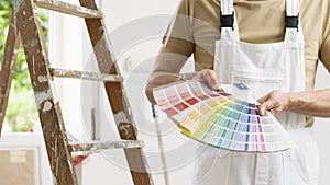 Hands of house painter man decorator choose the color using the sample swatch, work of the house to renovate, a wooden ladder and