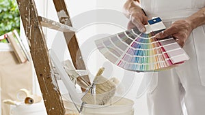 Hands of house painter man decorator choose the color using the sample swatch, work of the house to renovate, a wooden ladder with photo