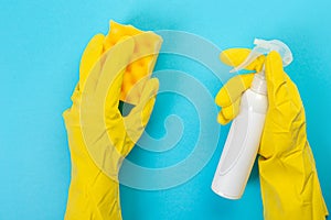 The hands of a housewife in yellow rubber protective gloves hold a bottle of household chemicals and a rag. Detergent for various