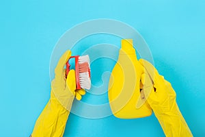 The hands of a housewife in yellow rubber protective gloves hold a bottle of household chemicals and a rag. Detergent for various