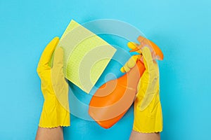 The hands of a housewife in yellow rubber protective gloves hold a bottle of household chemicals and a rag. Detergent for various