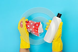 The hands of a housewife in yellow rubber protective gloves hold a bottle of household chemicals and a rag. Detergent for various