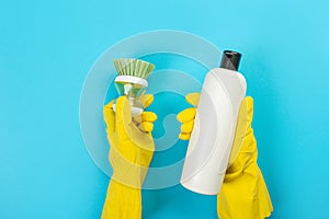 The hands of a housewife in yellow rubber protective gloves hold a bottle of household chemicals and a rag. Detergent for various