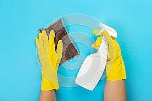 The hands of a housewife in yellow rubber protective gloves hold a bottle of household chemicals and a rag. Detergent for various