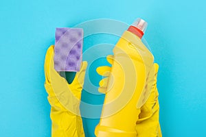 The hands of a housewife in yellow rubber protective gloves hold a bottle of household chemicals and a rag. Detergent for various