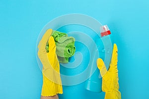 The hands of a housewife in yellow rubber protective gloves hold a bottle of household chemicals and a rag. Detergent for various