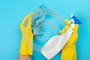 The hands of a housewife in yellow rubber protective gloves hold a bottle of household chemicals and a rag. Detergent for various