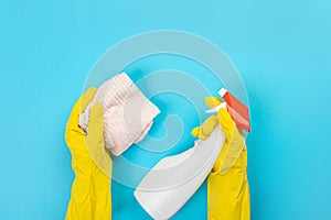 The hands of a housewife in yellow rubber protective gloves hold a bottle of household chemicals and a rag. Detergent for various