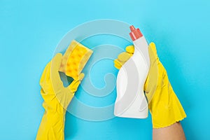 The hands of a housewife in yellow rubber protective gloves hold a bottle of household chemicals and a rag. Detergent for various