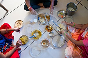 Hands of indian men and women having traditional gujarati thali  lunch on floor for being of low caste