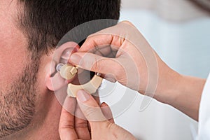 Hands inserting a hearing aid into a man's ear
