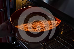 hands inserting the pan with the mix of biscuit crumbs, sugar and butter into the oven to bake the base of a cheesecak