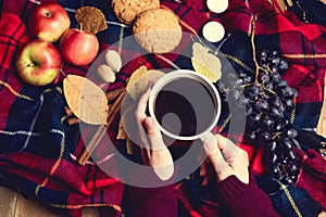 Hands keeping cup of coffee Apple Cookies Cinnamon Grape Wooden background Autumn woolen blanket Autumn lifestyle concept Top view