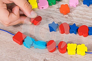 Hands of kid making bracelet from thread and colored beads. Development of kids motor skills, coordination and logical thinking