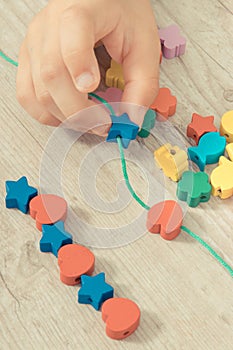 Hands of kid making bracelet from thread and colored beads. Development of kids motor skills, coordination and logical thinking