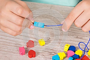 Hands of kid making bracelet from thread and colored beads. Development of kids motor skills, coordination and logical thinking