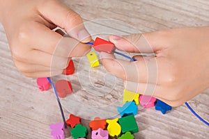 Hands of kid making bracelet from thread and colored beads. Development of kids motor skills, coordination and logical thinking