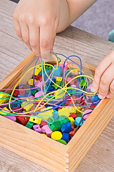Hands of kid playing thread and colorful beads used to making bracelets. Development of kids motor skills and logical thinking