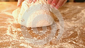 Hands kneading ball of dough on a floury surface