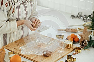 Hands kneading gingerbread dough on wooden board with rolling pin, golden metal cutters, cooking spices, festive decorations in
