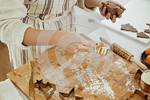 Hands kneading gingerbread dough on wooden board with rolling pin, golden metal cutters, cooking spices, festive decorations in