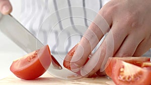 Hands with a knife cut a tomato into pieces in slow motion