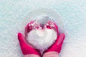 Hands in knitted mittens with a heart made of snow on a winter day. ... Snowy heart in hands. Human hands in warm red