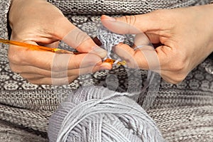 Hands knitting with crochet hook and grey yarn
