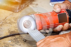 Hands of laborer holding electric angle grinder working chamfer at construction site with sun flare background