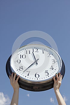 Hands lifting big clock outdoors