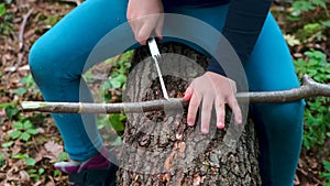 Hands of little girl or boy using a Swiss knife, sawing a piece of wood in the forest, nobody