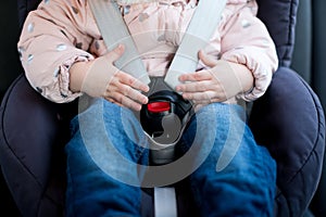Hands of a little girl lie on the seat belt buckle of a child seat