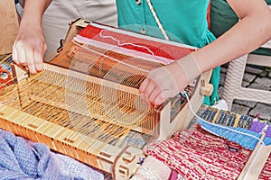 Hands of little girl weaving small rug on manual table loom at outdoors workshop on weaving.