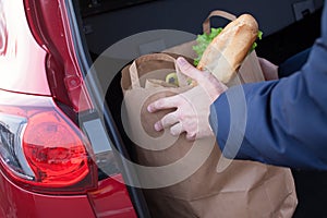 Hands loading a shopping bag in car trunk