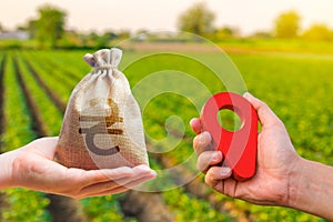 Hands with location pin and ukrainian hryvnia money bag. Land market. Estimation cost of plots. Agriculture agribusiness.