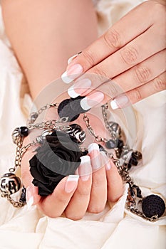 Hands with long artificial french manicured nails holding a necklace and black rose flower