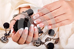 Hands with long artificial french manicured nails holding a necklace and black rose flower