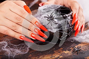 Hands with long artificial manicured nails colored with orange nail polish and Halloween decorations