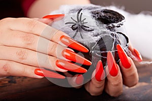 Hands with long artificial manicured nails colored with orange nail polish and Halloween decorations